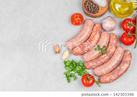 Fresh sausages arranged on a gray countertop with tomatoes, garlic, onion, parsley, black pepper, and olive oil in a rustic kitchen setting 142303398