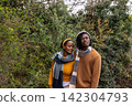 African American couple standing close together in park, wearing knit scarves and warm sweaters 142304793