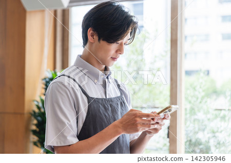 A male cafe staff member taking orders via smartphone A male cafe staff member taking orders via smartphone 142305946