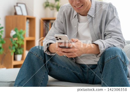A young man looking at his smartphone at home A young man looking at his smartphone at home 142306358