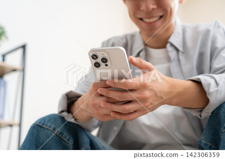 A young man looking at his smartphone at home A young man looking at his smartphone at home 142306359