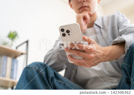 A young man looking at his smartphone at home A young man looking at his smartphone at home 142306362