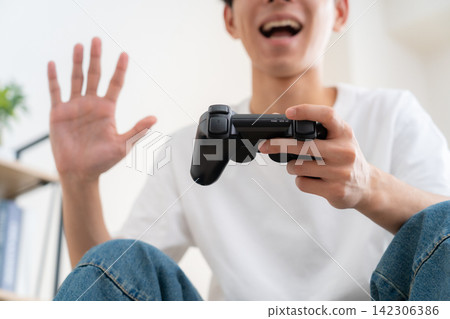 一個年輕人在家玩電子遊戲 142306386