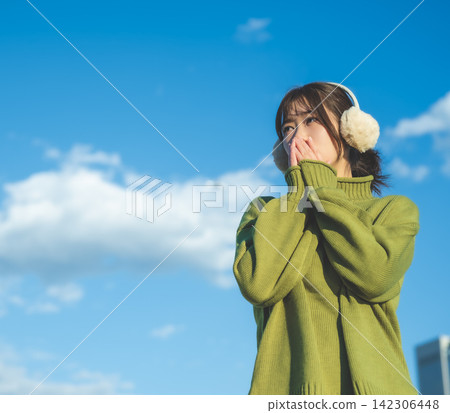 A woman wearing earmuffs covers her face, looking cold. A woman wearing earmuffs covers her face, looking cold. 142306448