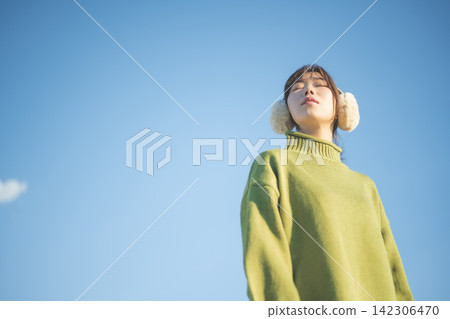 A woman wearing earmuffs looks up at the sky and closes her eyes. A woman wearing earmuffs looks up at the sky and closes her eyes. 142306470