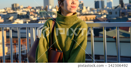 一位身穿針織毛衣的女士在城市屋頂放鬆休息。 一位身穿針織毛衣的女士在城市屋頂放鬆休息。 142306492
