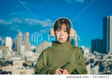 A woman wearing earmuffs and a city skyline. A woman wearing earmuffs and a city skyline. 142306513