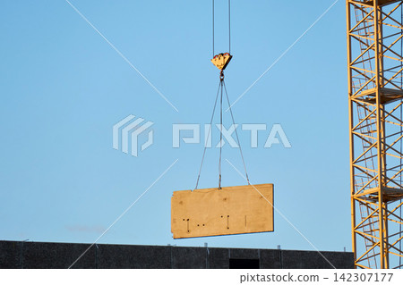 Tower crane hoisting precast concrete panel at building site Tower crane hoisting precast concrete panel at building site 142307177