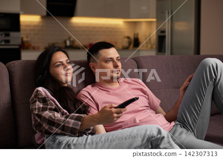 Couple relaxing on couch watching tv at home Couple relaxing on couch watching tv at home 142307313