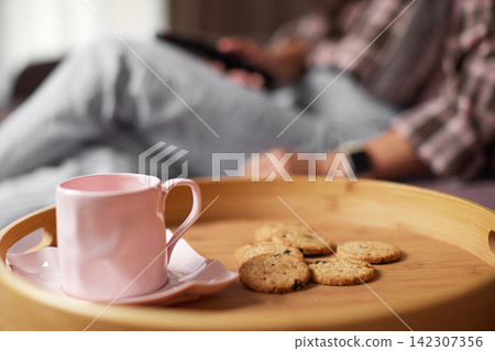 Person relaxing with coffee and cookies on tray 142307356