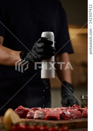 Chef seasoning raw beef meat with salt grinder Chef seasoning raw beef meat with salt grinder 142307412