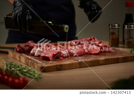 Chef pouring olive oil on raw beef steak Chef pouring olive oil on raw beef steak 142307413