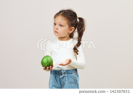 Young girl holding avocado looking curious about healthy eating Young girl holding avocado looking curious about healthy eating 142307651