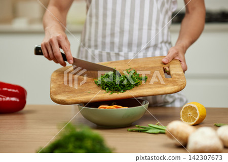 Woman cooking fresh herbs and vegetables in kitchen Woman cooking fresh herbs and vegetables in kitchen 142307673