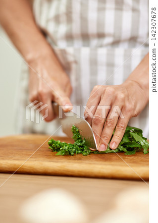 Hands chopping fresh green vegetables on cutting board Hands chopping fresh green vegetables on cutting board 142307678