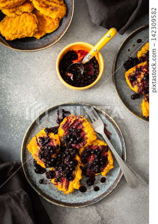 Millet pancakes are arranged on a plate and topped with currant sauce. The scene displays a simple breakfast setting at home in the morning Millet pancakes are arranged on a plate and topped with currant sauce. The scene displays a simple breakfast setting at home in the morning 142309582