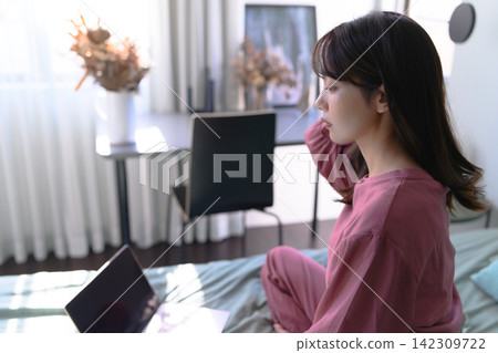 一名女子在床上使用筆記型電腦。 142309722
