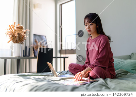 使用膝上型計算機的婦女在床上 使用膝上型計算機的婦女在床上 142309724