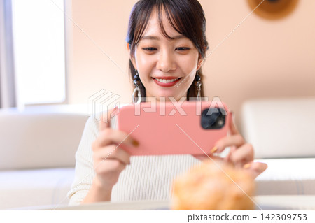 一位女士一邊用智慧型手機拍攝甜點,一邊露出笑容。 一位女士一邊用智慧型手機拍攝甜點,一邊露出笑容。 142309753