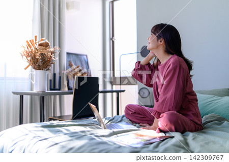 A woman relaxing in bed and looking at her laptop. A woman relaxing in bed and looking at her laptop. 142309767