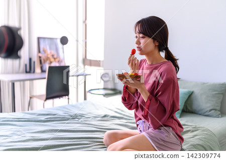 一個女人在床上吃櫻桃番茄 一個女人在床上吃櫻桃番茄 142309774
