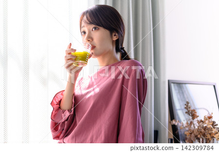 A young woman drinking green juice in her room, showing her health consciousness. A young woman drinking green juice in her room, showing her health consciousness. 142309784