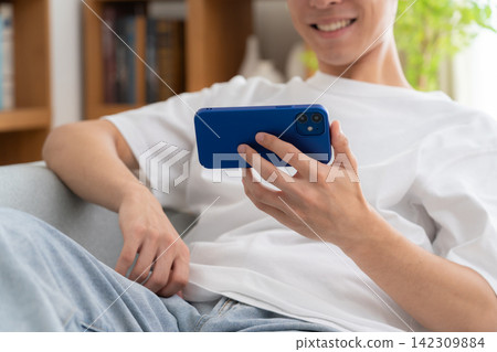 A young man looking at his smartphone at home A young man looking at his smartphone at home 142309884