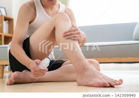 A young man removes hair from his legs at home. A young man removes hair from his legs at home. 142309940