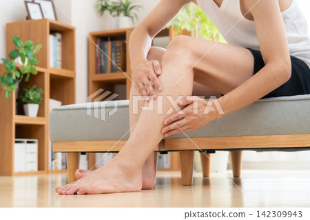 A young man removes hair from his legs at home. A young man removes hair from his legs at home. 142309943