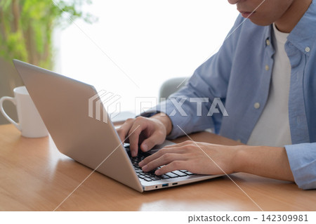 A young man at home using his computer. A young man at home using his computer. 142309981