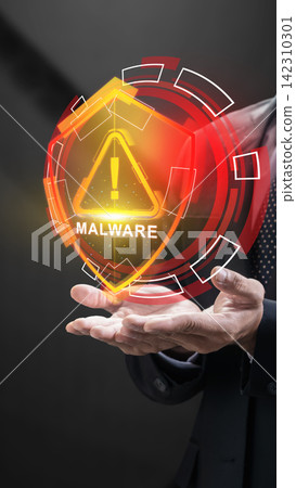 Businessman displaying a glowing orange holographic shield with a malware warning alert, representing cybersecurity threats and data defense. Cybersecurity concept Businessman displaying a glowing orange holographic shield with a malware warning alert, representing cybersecurity threats and data defense. Cybersecurity concept 142310301