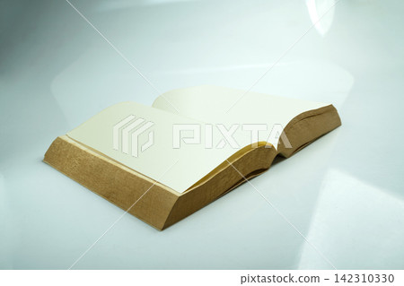 An open blank book with white pages lying on a clean light blue surface. Study or education concept An open blank book with white pages lying on a clean light blue surface. Study or education concept 142310330