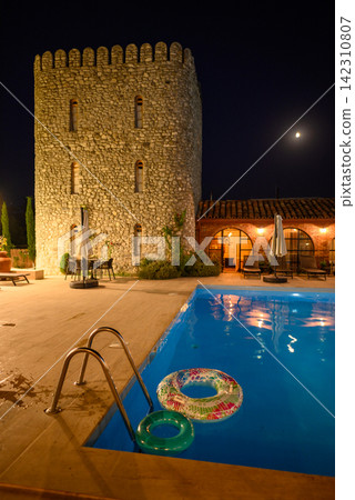 A serene night scene at a luxurious outdoor resort featuring a stone tower and vibrant blue swimming pool A serene night scene at a luxurious outdoor resort featuring a stone tower and vibrant blue swimming pool 142310807