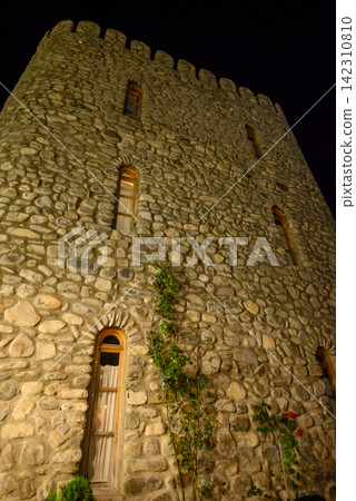 A low-angle nighttime photograph capturing an ancient stone tower with textured stonework and arched windows 142310810