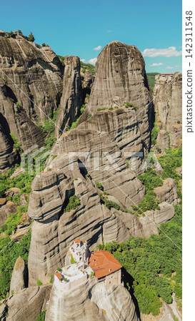 Aerial vertical view of Saint Nicholas Anapausas monastery built on high cliff rocks in Meteora complex surrounded by green trees vertical stock photo 142311548