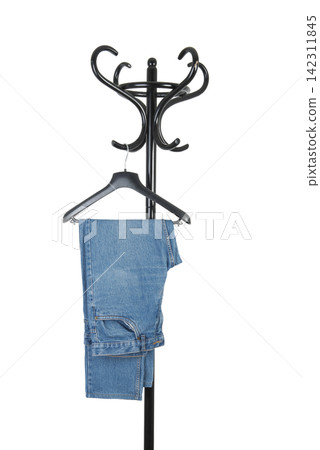 A pair of blue jeans hangs from a black hanger on a black coat rack A pair of blue jeans hangs from a black hanger on a black coat rack 142311845
