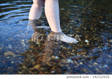 Bare foot stepping through shallow river water with colorful pebble Bare foot stepping through shallow river water with colorful pebble 142312010