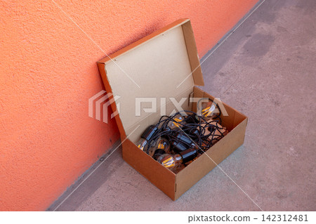 String of vintage filament light bulbs inside a cardboard box. Decorative LED garland for party lighting and home decor. Industrial style electric lamp cord for celebration. String of vintage filament light bulbs inside a cardboard box. Decorative LED garland for party lighting and home decor. Industrial style electric lamp cord for celebration. 142312481