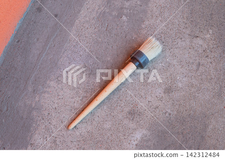 Round paintbrush with wooden handle lying on concrete floor. Tool for painting, renovation, and DIY construction project. Artistic instrument for creative hobby, home improvement, and repair. Round paintbrush with wooden handle lying on concrete floor. Tool for painting, renovation, and DIY construction project. Artistic instrument for creative hobby, home improvement, and repair. 142312484