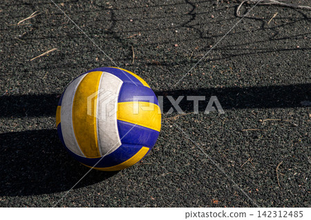 Volleyball on an outdoor court. Athletic equipment resting on a rubber surface with net shadow. Sport gear for professional competition, summer team game and active recreation training. 142312485