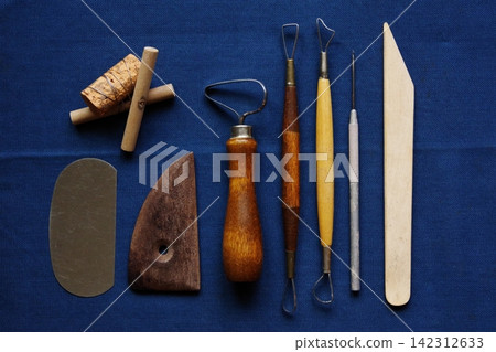 Wooden and metal sculpting tools and other implements are laid out on a navy blue cloth. Wooden and metal sculpting tools and other implements are laid out on a navy blue cloth. 142312633