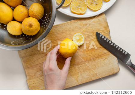 Hand Cutting a Fresh Garden Lemon on a Wooden Cutting Board with Slices on a White Plate Hand Cutting a Fresh Garden Lemon on a Wooden Cutting Board with Slices on a White Plate 142312660