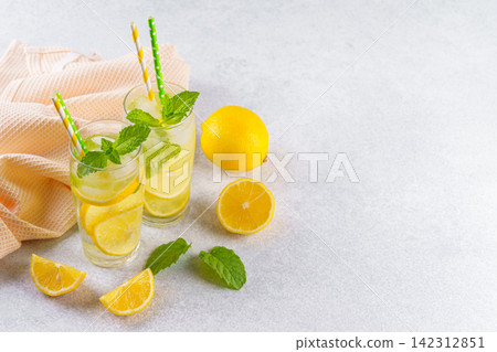 Cold homemade lemonade with fresh lemon, mint and ice in glasses on gray background, copy space Cold homemade lemonade with fresh lemon, mint and ice in glasses on gray background, copy space 142312851