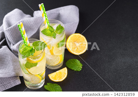Cold homemade lemonade with fresh lemon, mint and ice in glasses on black background, copy space Cold homemade lemonade with fresh lemon, mint and ice in glasses on black background, copy space 142312859