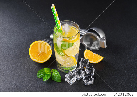 Cold homemade lemonade with fresh lemon, mint and ice in glass on black textured stone background 142312862