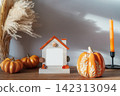 Cozy warm autumn home interior - decorative orange ceramic pumpkins, house's shaped photo frame with copy space, candles, dried flowers on the wooden console. Seasonal hygge home fall decor 142313094