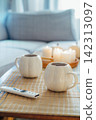 Autumn fall mood composition for hygge home decor. White pumpkin's shaped cups with hot drink, burning candles, remote controller on coffee table in living room. Movie night at home. Cozy relax time 142313097