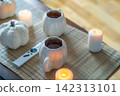 Autumn fall mood composition for hygge home decor. White pumpkin's shaped cups with hot drink, burning candles, remote controller on coffee table in living room. Movie night at home. Cozy relax time 142313101