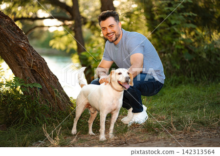 Man petting happy Labrador dog in park enjoying nature 142313564