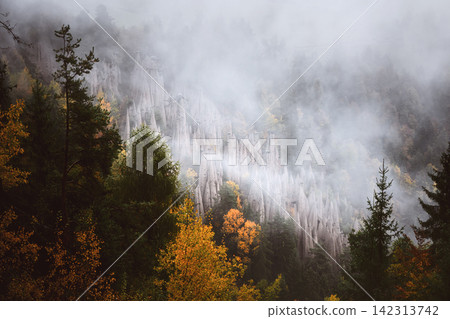 Autumn forest covered by drifting fog beneath the earth pyramids Autumn forest covered by drifting fog beneath the earth pyramids 142313742
